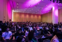 Large audience seated in a brightly lit auditorium for a conference or tech event.