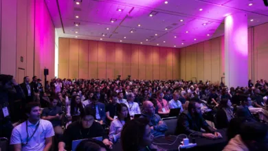 Large audience seated in a brightly lit auditorium for a conference or tech event.