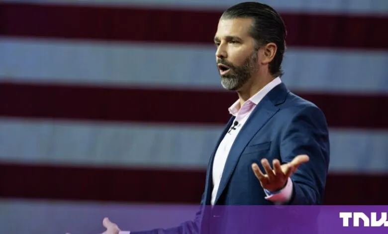 Donald Trump Jr. speaking passionately with gestures in front of an American flag.