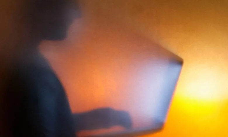 Silhouette of a person working on a laptop against a glowing orange background.