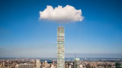 A lone fluffy white cloud hovers perfectly directly above a tall skyscraper in New York City.