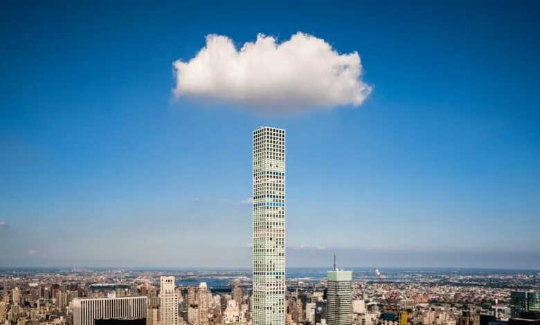 A lone fluffy white cloud hovers perfectly directly above a tall skyscraper in New York City.