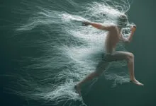A man runs midair as countless white wires trail dynamically behind him in a greenish space.