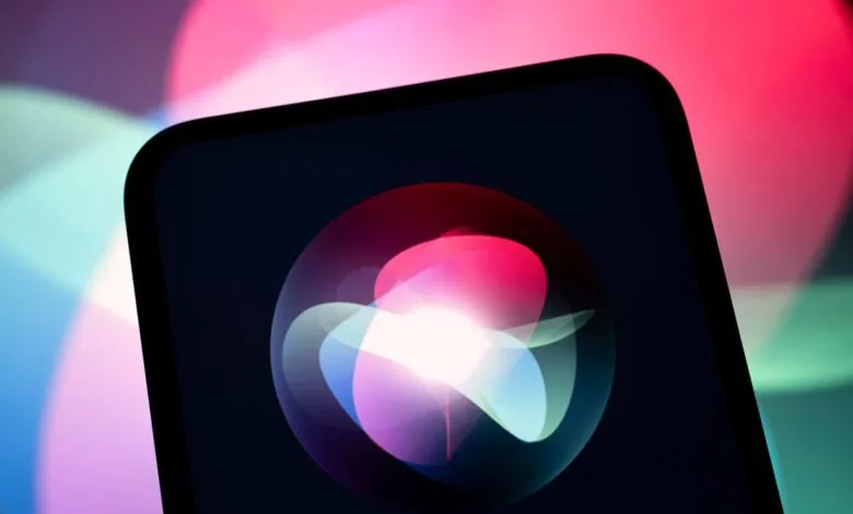Close-up of a smartphone displaying the glowing multicolored Siri animation on a dark background.