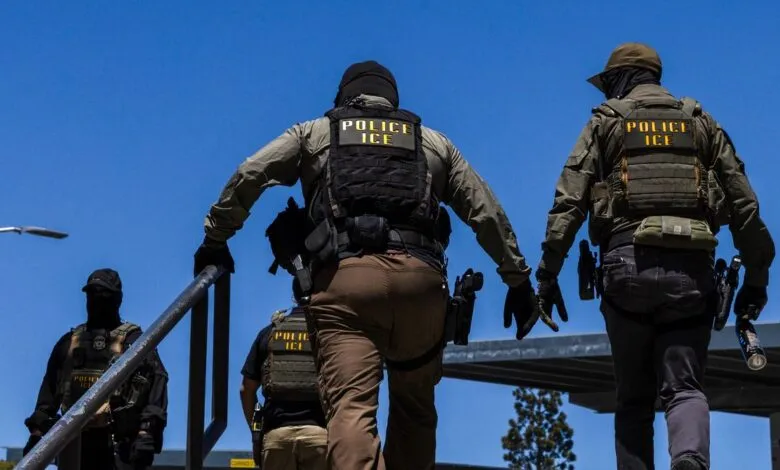 Low angle view of armed ICE police officers in tactical gear walking up outdoor stairs.