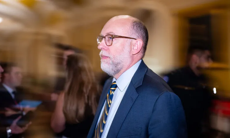 OMB Director Russell Vought wearing a dark suit and glasses, walking indoors.