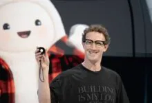 Meta CEO Mark Zuckerberg holding a small black device in front of a large cartoon mascot display.