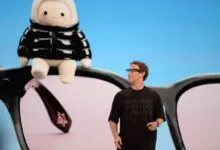 Meta CEO Mark Zuckerberg presents on stage in front of a giant graphic of smart glasses and a plush toy.