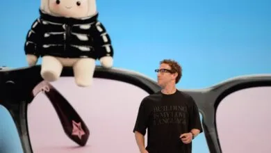 Meta CEO Mark Zuckerberg presents on stage in front of a giant graphic of smart glasses and a plush toy.