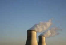 Two nuclear power plant cooling towers releasing white steam against a clear blue sky.