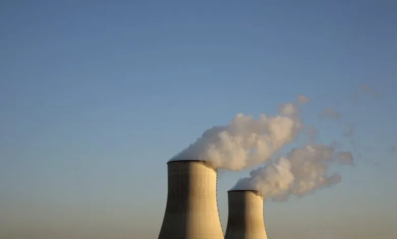 Two nuclear power plant cooling towers releasing white steam against a clear blue sky.