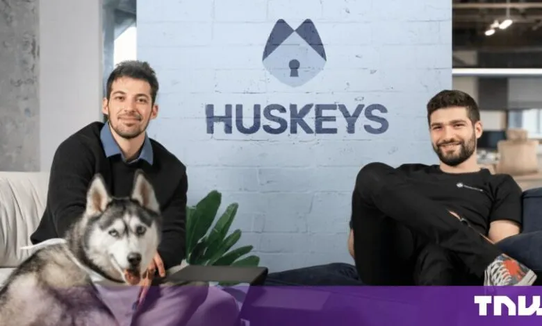 Two startup founders posing in an office with a Husky dog in front of a painted brick wall with the Huskeys logo.