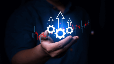 A person holding glowing white gears with upward arrows and financial charts in the background.