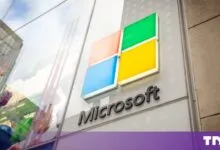 The Microsoft logo mounted on a glass storefront facade outdoors.