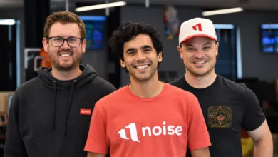 Three smiling men standing together inside a modern office, wearing casual clothing and branded apparel.