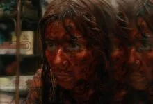 A woman's face covered in blood, reflected in a triple mirror, with a terrified expression.