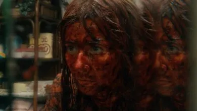 A woman's face covered in blood, reflected in a triple mirror, with a terrified expression.