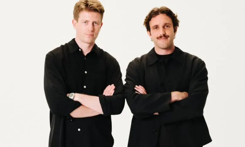 Two men standing side by side against a white background with arms crossed, wearing black shirts.