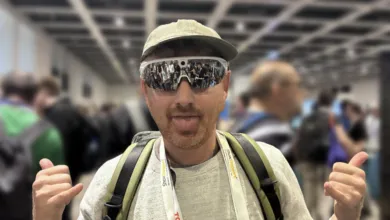 A man wearing futuristic smart glasses and a baseball cap playfully sticks out his tongue.