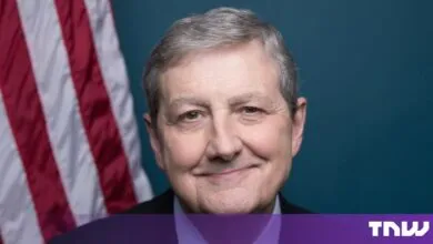 Official portrait of US Senator John Kennedy smiling against a dark teal background with an American flag.