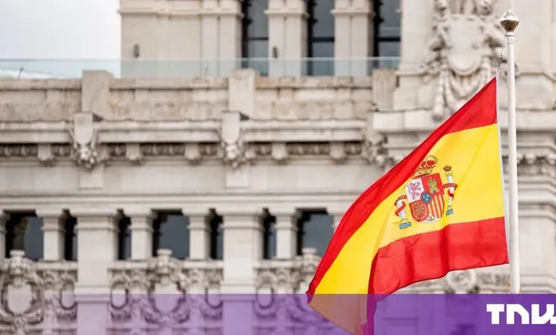The flag of Spain waving proudly in front of a majestic historic stone building.