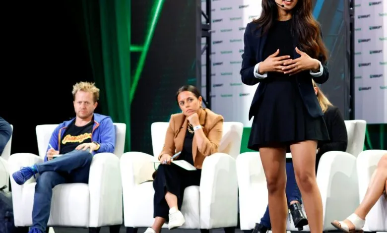 A woman speaks on stage during a TechCrunch Disrupt event while judges listen from white armchairs.