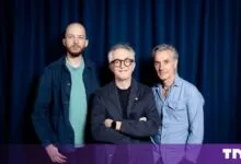 Three men posing together in front of a dark blue curtain backdrop.