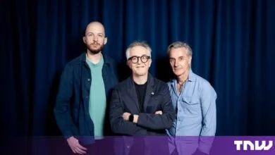 Three men posing together in front of a dark blue curtain backdrop.