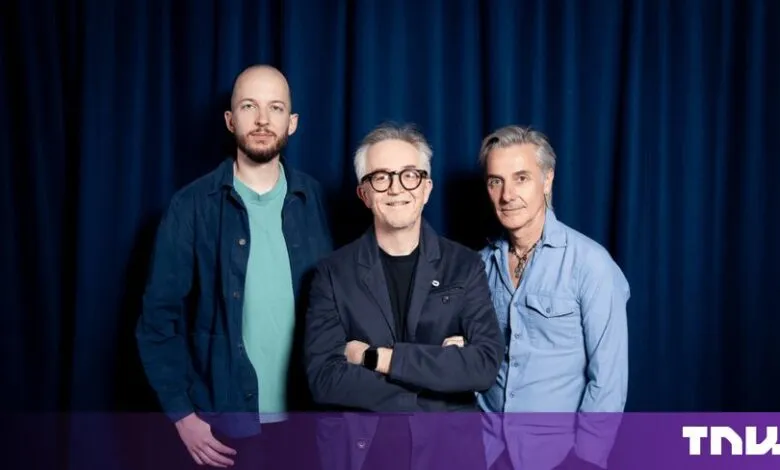 Three men posing together in front of a dark blue curtain backdrop.