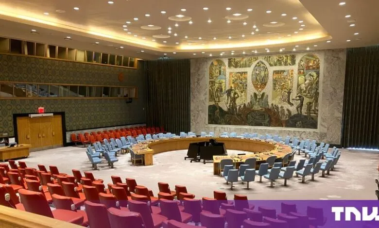 Empty United Nations Security Council Chamber featuring a horseshoe-shaped table and large mural.