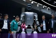 A humanoid AI robot stands prominently on a convention floor, surrounded by onlookers.