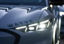Close-up of a silver autonomous vehicle with the Wayve logo and glowing headlights.