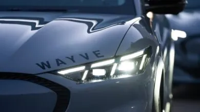 Close-up of a silver autonomous vehicle with the Wayve logo and glowing headlights.