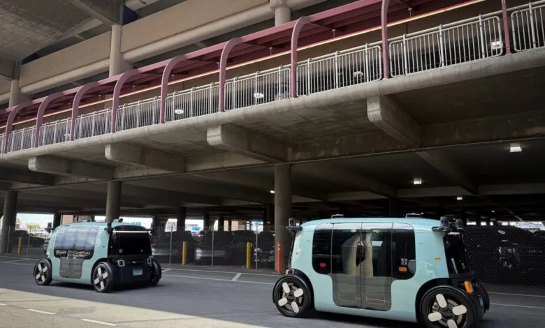 Two autonomous Zoox robotaxis parked under a concrete parking structure.