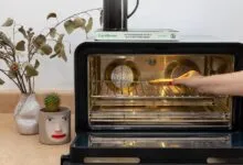 Hand placing a slice of bread onto the rack inside a modern, sleek countertop convection oven.