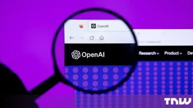 Magnifying glass focused on the OpenAI website displayed on a screen against a purple background.