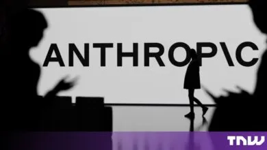 Silhouette of a person walking past a large screen displaying the Anthropic company logo