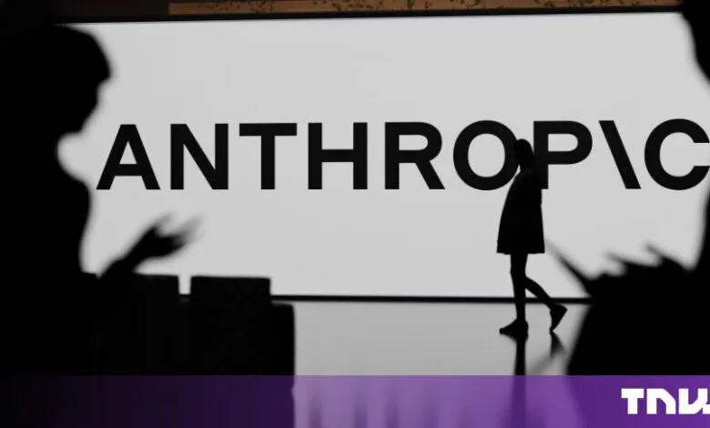 Silhouette of a person walking past a large screen displaying the Anthropic company logo