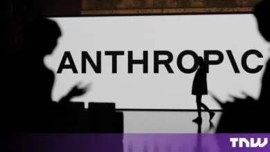 Silhouette of a person walking past a large screen displaying the Anthropic company logo in black and white.