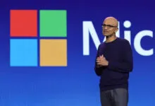 Microsoft CEO Satya Nadella speaking on stage in front of a large Microsoft logo.