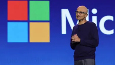 Microsoft CEO Satya Nadella speaking on stage in front of a large Microsoft logo.
