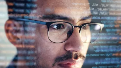 Close-up of a software developer wearing glasses with code reflected on his face.