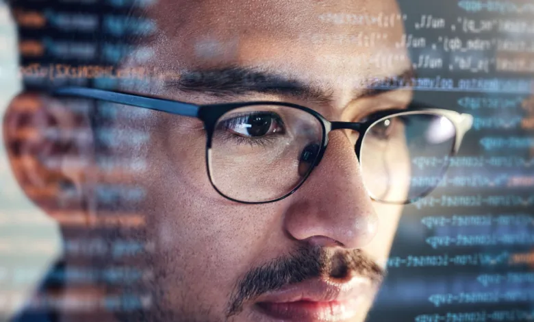 Close-up of a software developer wearing glasses with code reflected on his face.