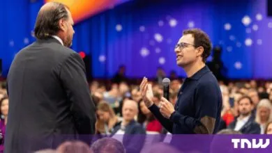 Marc Benioff listens as Dario Amodei speaks with a microphone at an event