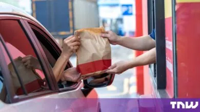 A customer receives a takeaway food bag through a car window at a fast-food drive-thru.