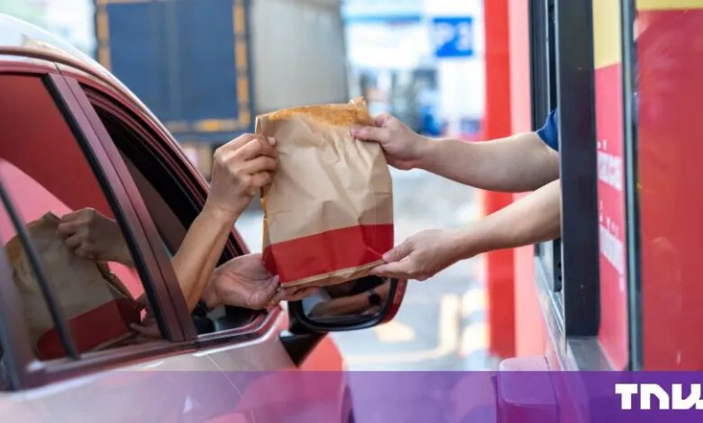 A customer receives a takeaway food bag through a car window at a fast-food drive-thru.