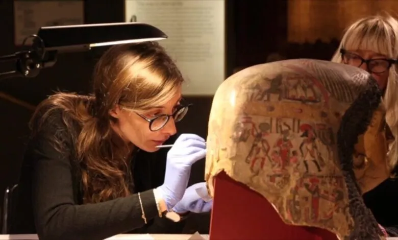 Conservators carefully restore an ancient Egyptian artifact with delicate tools in a museum lab.