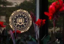 Golden FBI seal mounted on a dark stone wall, framed by vibrant red flowers in the foreground.