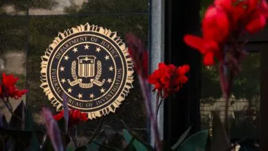 Golden FBI seal mounted on a dark stone wall, framed by vibrant red flowers in the foreground.