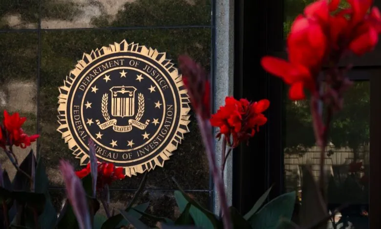 Golden FBI seal mounted on a dark stone wall, framed by vibrant red flowers in the foreground.